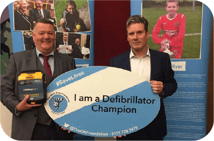 Photograph of Mark King and MP Sir Keir Starmer, holding up a "I am a Defibrillator Champion" sign